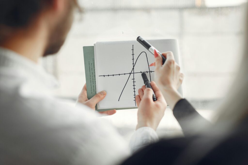 Two professionals discussing a parabola graph on a notebook, promoting teamwork and collaboration.